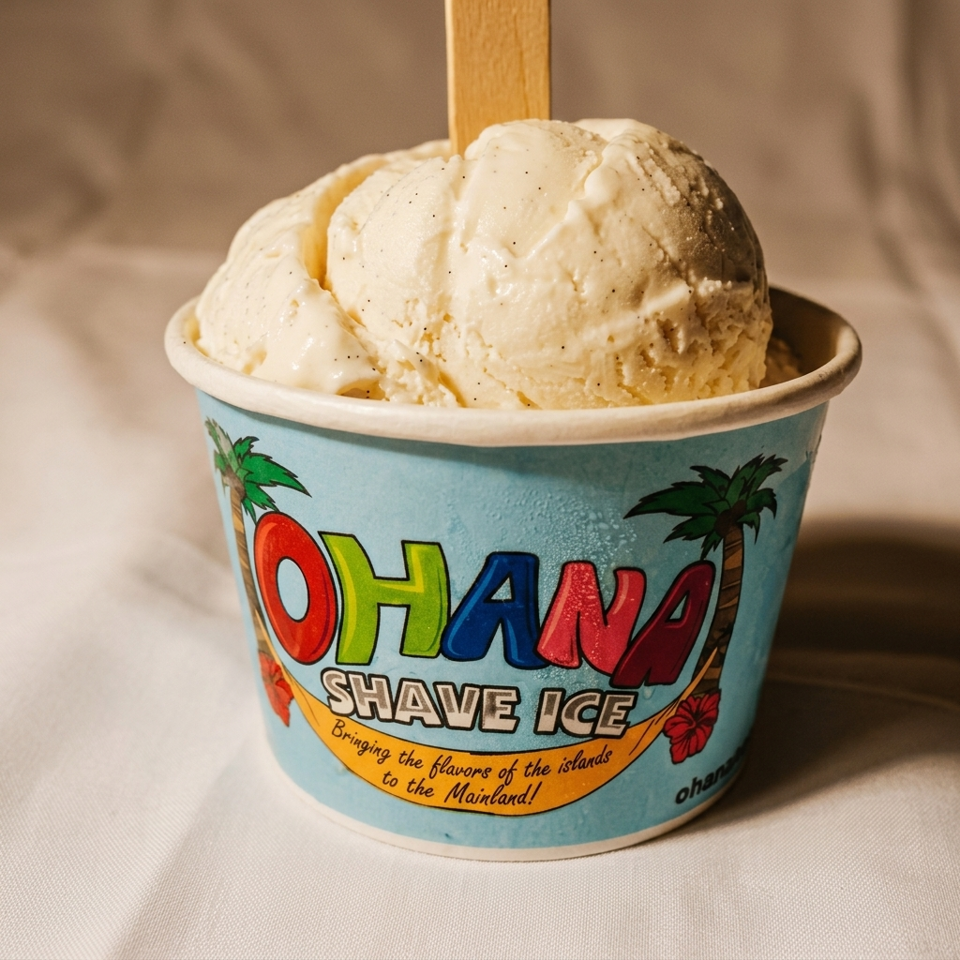 Two scoops of vanilla ice cream in a colorful Ohana Shave Ice cup with a wooden spoon.